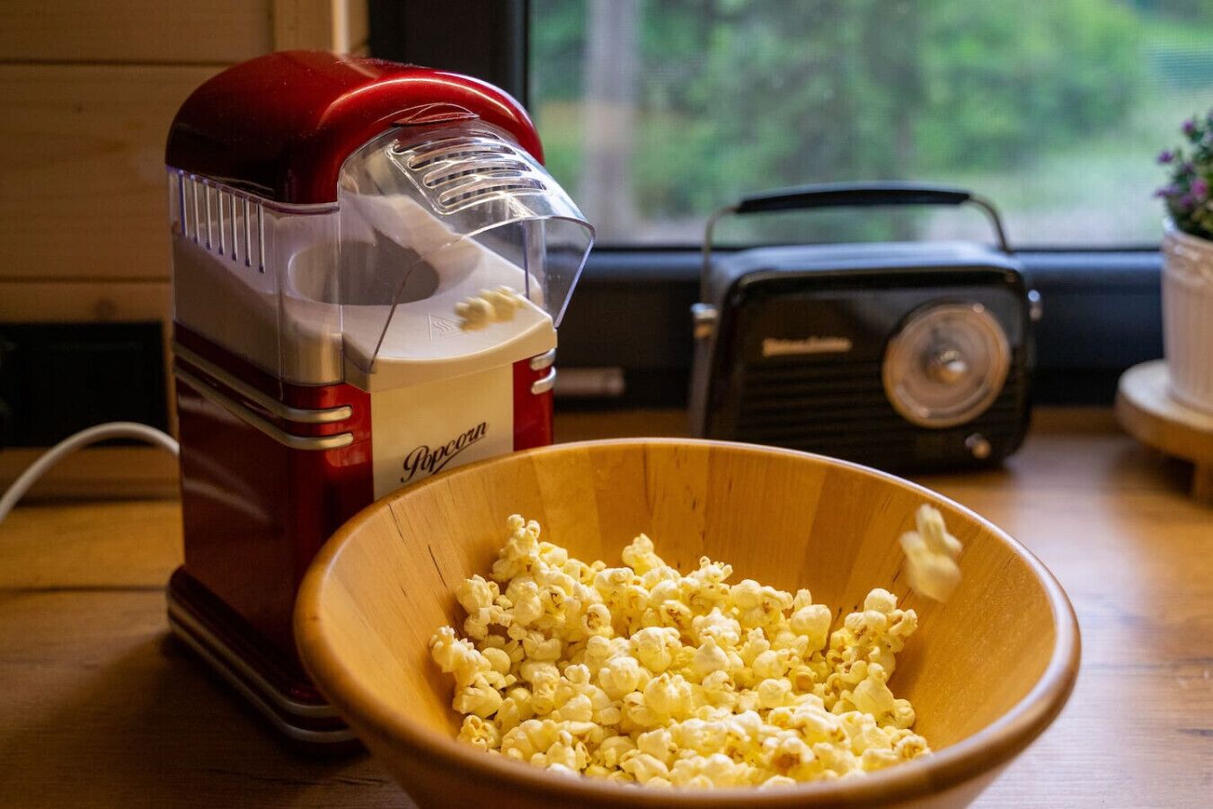 A wooden bowl filled with popcorn next to a red popcorn machine.