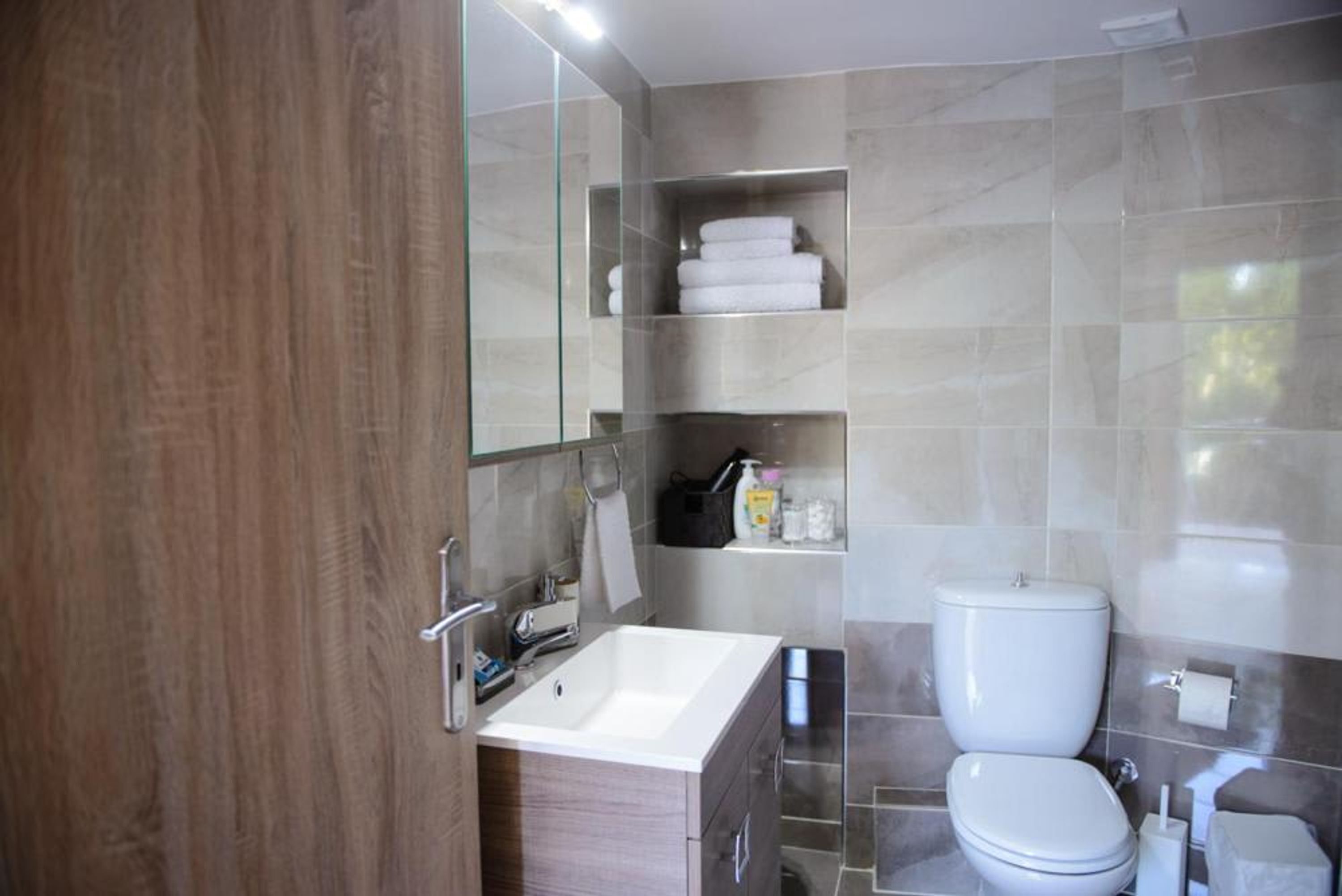 Une salle de bain moderne avec un meuble-lavabo en bois, un lavabo blanc, des toilettes et une douche à parois de verre.