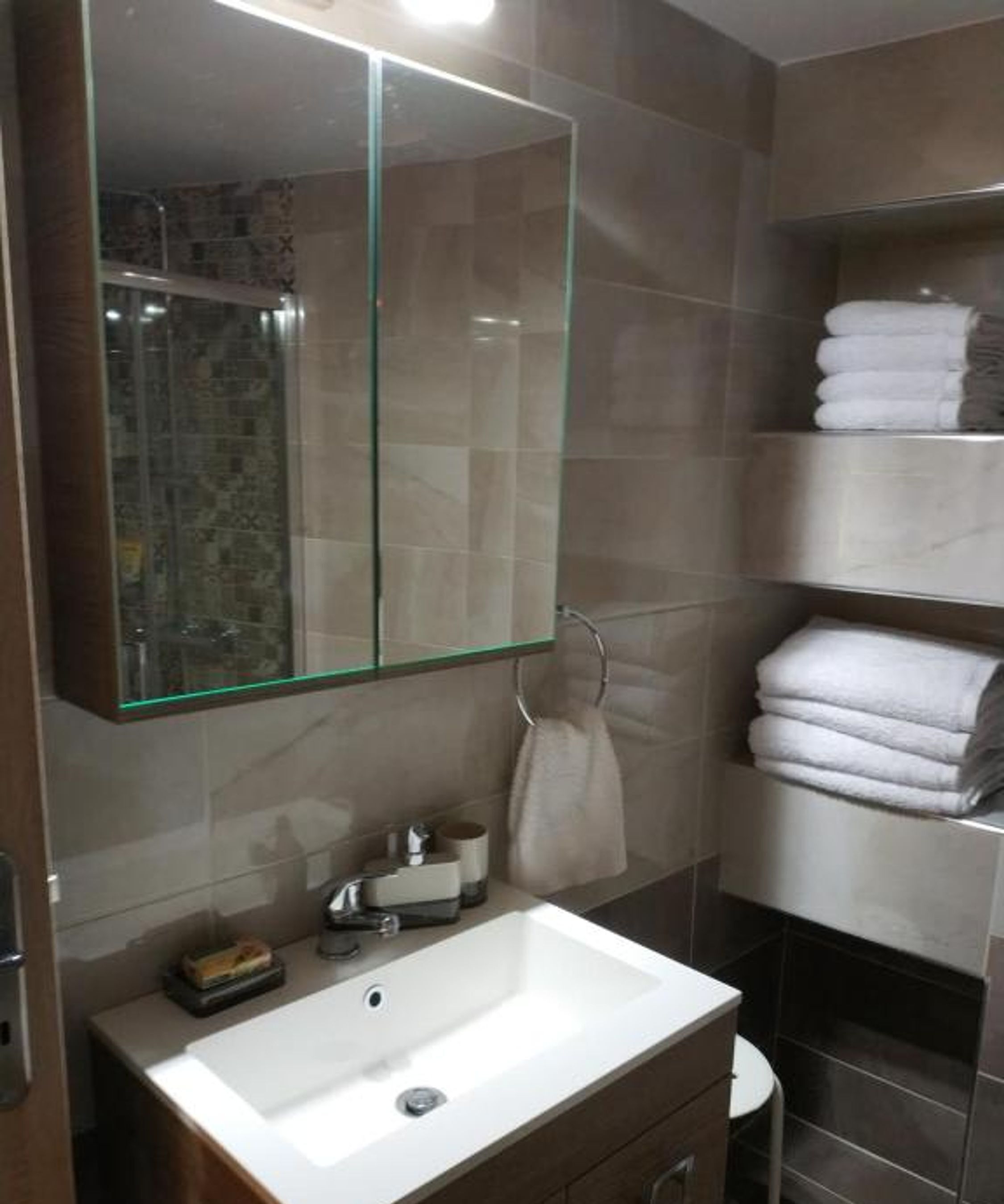 A bathroom with a large mirror, a sink, and a towel rack.