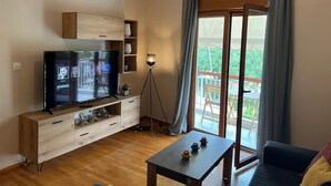 Una sala de estar moderna con un televisor de pantalla plana, muebles de madera, una lámpara de pie y un balcón con vistas.