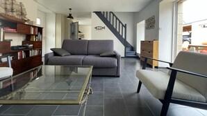 A modern living room with a sofa, a glass coffee table, and a bookshelf. There is a staircase leading to another level. - Pink Granite Coast in Brittany: Comfortable Home with Wi-Fi (Trébeurden)