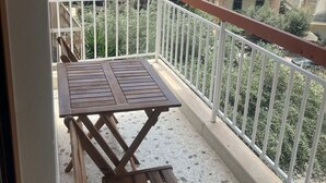 A balcony with a wooden table and two chairs, a white railing, and a view of the cityscape. - Sunny Coastal Escape in Alimos (Alimos)