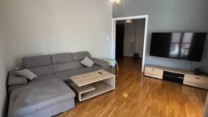 A modern living room with a grey sectional sofa, a wooden coffee table, a flat-screen TV, and a wooden floor. - Sunny Coastal Escape in Alimos (Alimos)