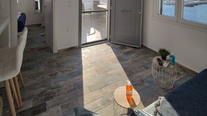 A spacious living area with a view of the sea, a sliding glass door leading to an outdoor balcony, and a modern interior design. - Alos Seafront Gem - Loutra Seaview Escape (Kithnos)