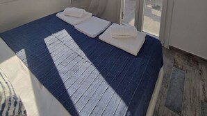 A bedroom with a large bed, a view of the sea through a sliding door, and a ceiling light. - Alos Seafront Gem - Loutra Seaview Escape (Kithnos)