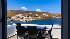 A balcony with wicker chairs and a table overlooking a coastal town with buildings and boats. - Alos Seafront Gem - Loutra Seaview Escape (Kithnos)