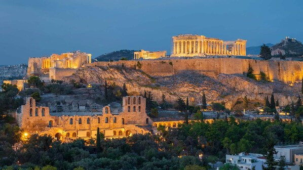 Ancient ruins with columns and a temple on a hill, overlooking a cityscape.