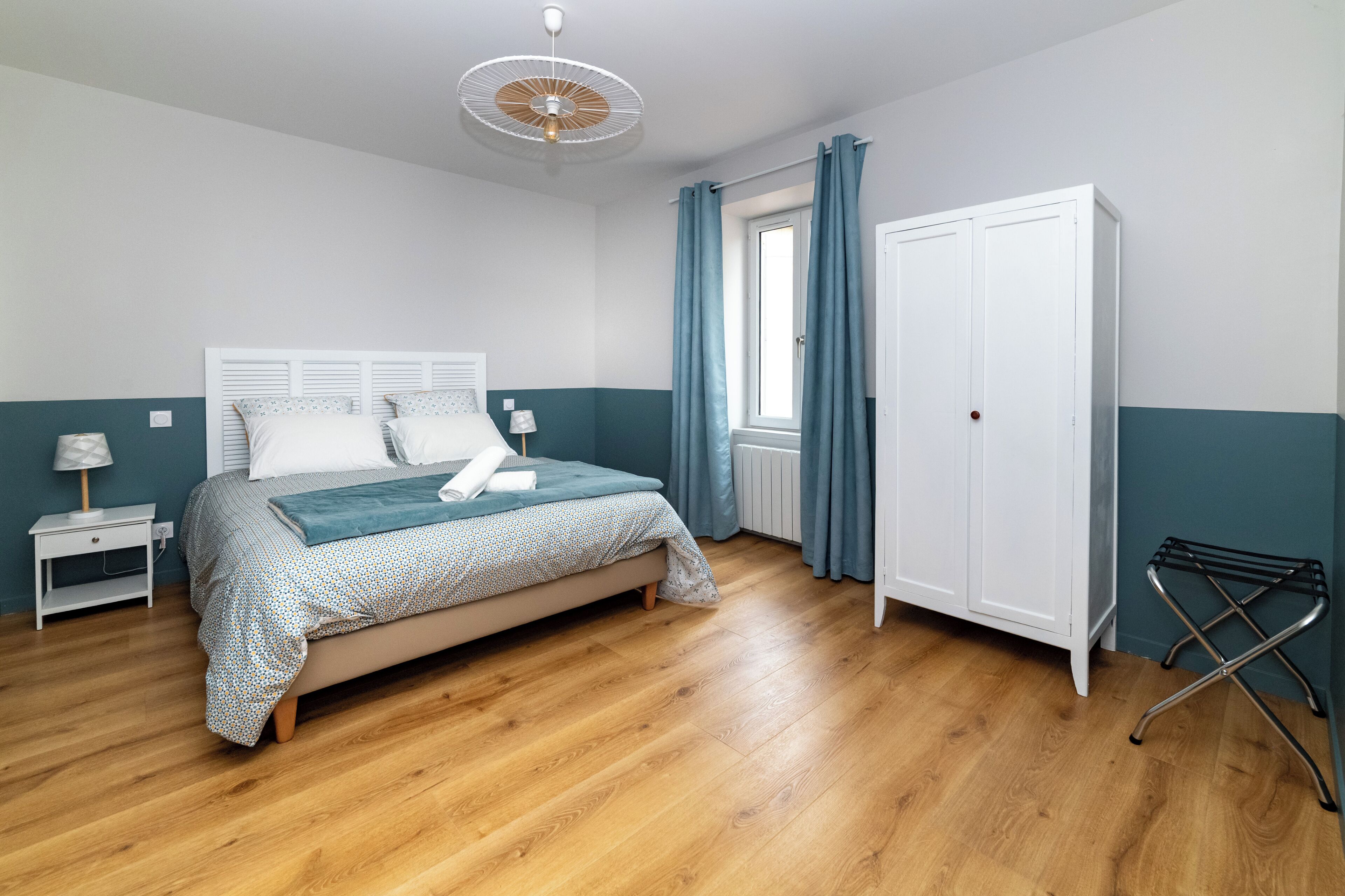 Een slaapkamer met een bed, een kledingkast, een nachtkastje, een lamp en een raam met gordijnen.