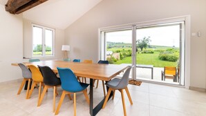 A dining area with a wooden table and colorful chairs, large windows with a view of a green landscape. - L'échappée Beaujolaise (Juliénas)