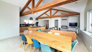 A spacious dining area with a wooden table and colorful chairs, a kitchen with modern appliances, and a cozy seating area with a sofa and TV. - L'échappée Beaujolaise (Juliénas)