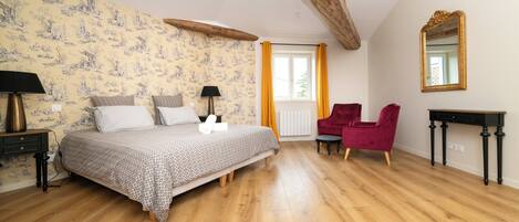 Un dormitorio con suelo de madera, una cama con ropa de cama estampada, un sillón rojo, una mesita de noche negra y un espejo en la pared.