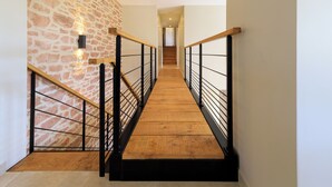 A wooden staircase with black railings, leading to a landing with a stone wall and recessed lighting. - L'échappée Beaujolaise (Juliénas)