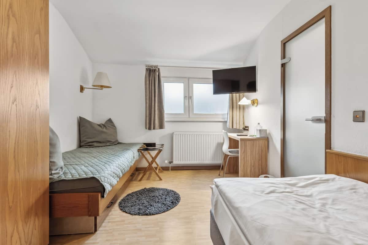A compact hotel room with a bed, a desk, a TV, and a window.