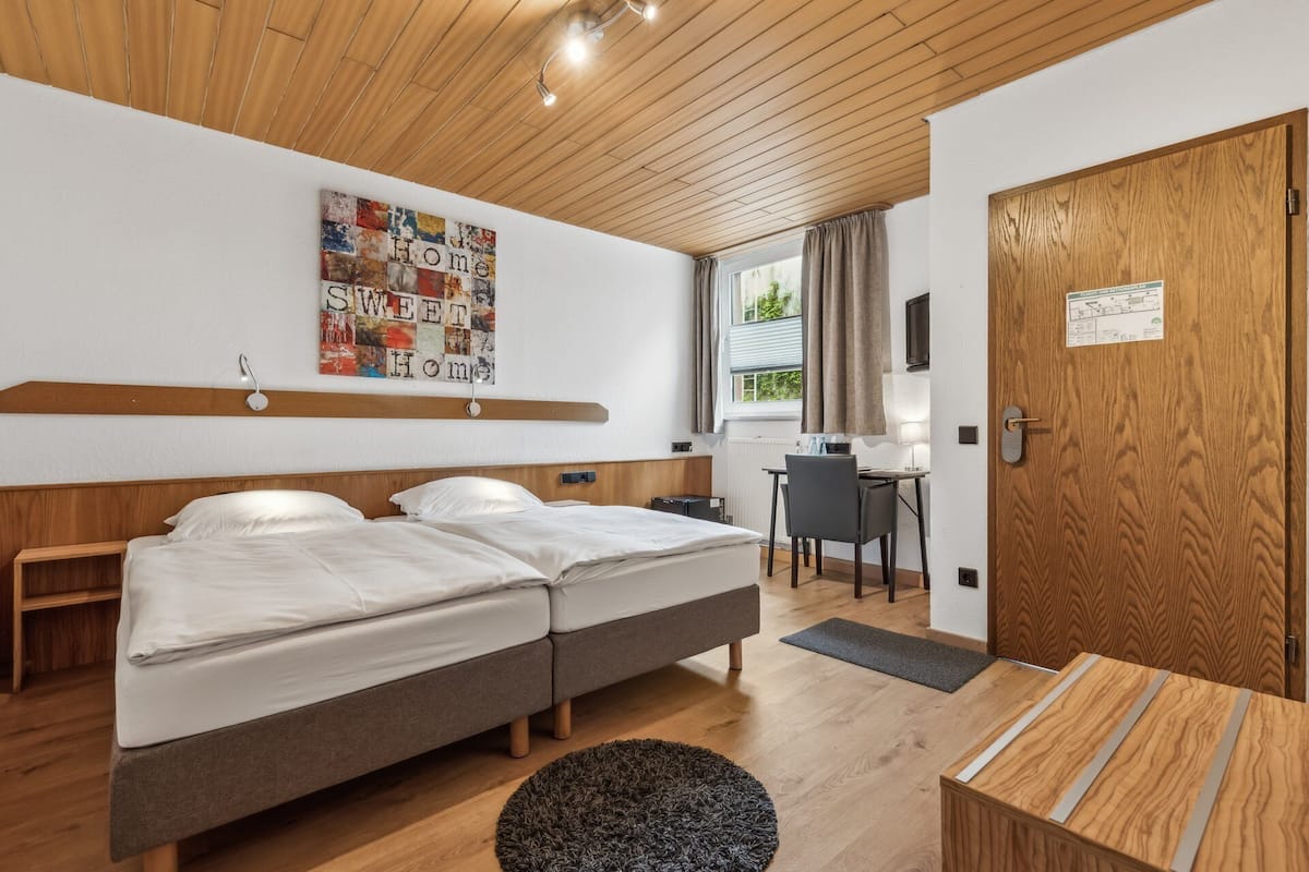 A modern hotel room with two beds, a desk, and a view of the outdoors.