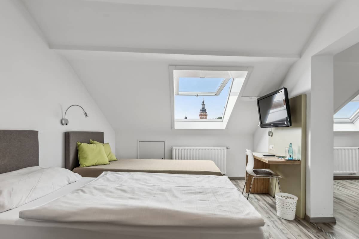 A modern, well-lit bedroom with two beds, a desk, a TV, and a skylight.