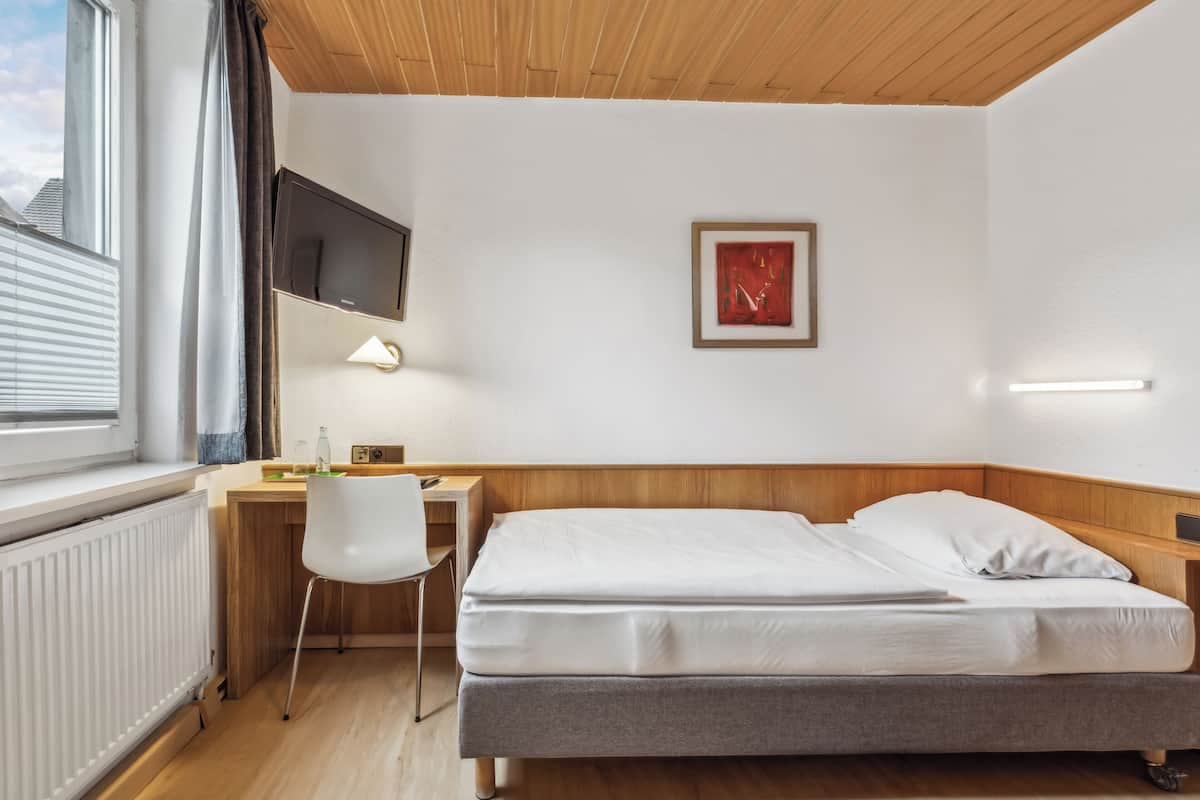 A hotel room with a bed, a desk, a chair, a TV, and a window with blinds.