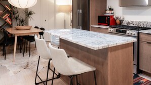 Een moderne keuken met een marmeren eiland, roestvrijstalen apparatuur en een eethoek met een houten tafel en stoelen.