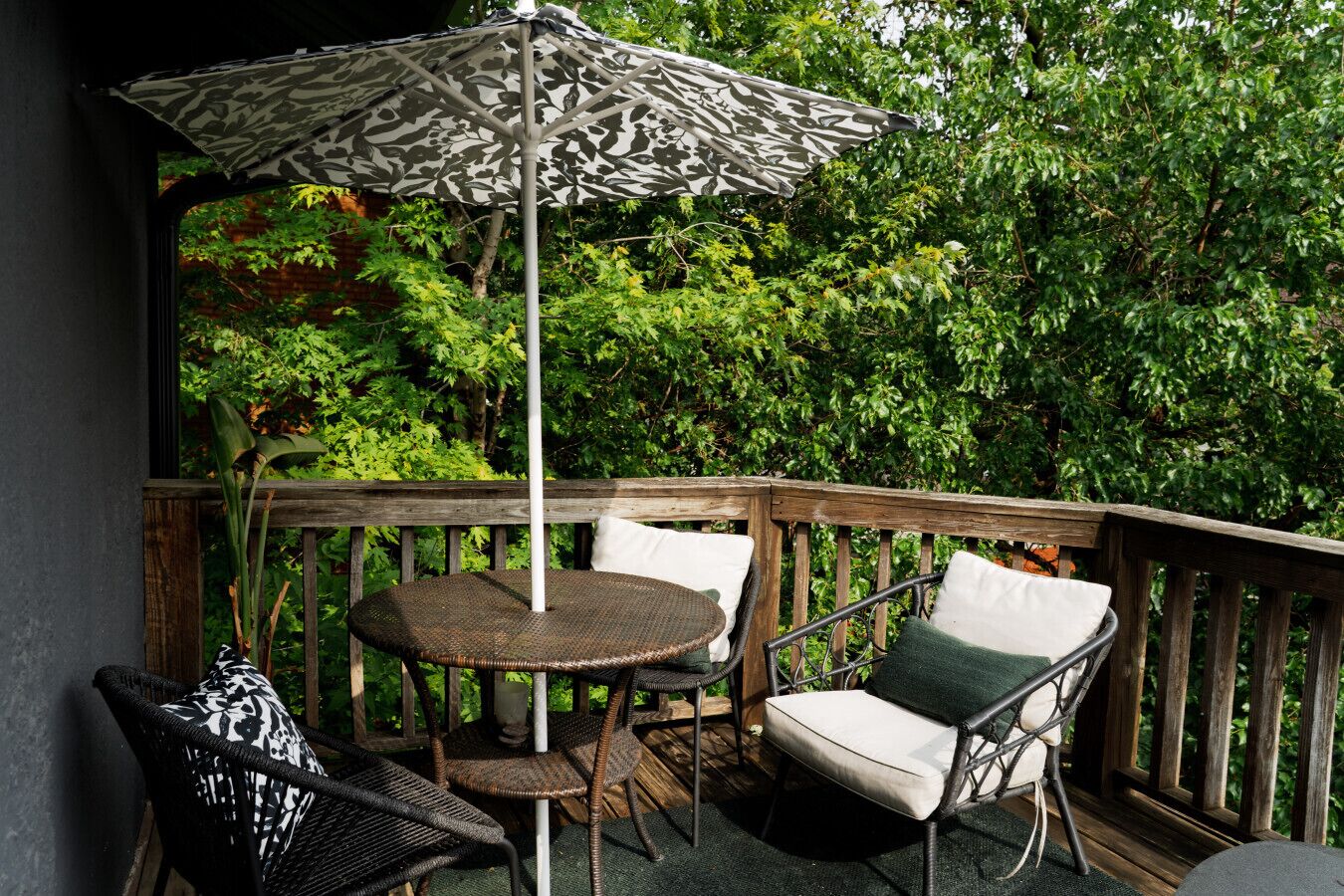 Une terrasse en bois agrémentée de meubles en osier, notamment une table ronde et deux chaises, ainsi qu’un parasol à motifs.