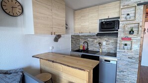 Cocina compacta con armarios de madera, microondas, lavamanos y una pequeña isla con taburetes.