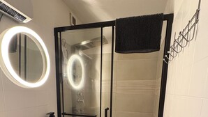 Un baño con ducha de vidrio, un espejo redondo con luz y un tocador de madera con lavamanos.