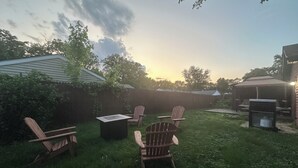 Un jardin avec un patio couvert, un barbecue et des fauteuils Adirondack.