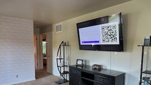 Un salon doté d’un téléviseur à écran plat fixé au mur, d’un meuble de rangement noir pour appareils multimédias et d’une étagère décorative sur laquelle est posée une lanterne.