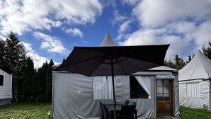A tent with a table and chairs set up on a wooden deck, surrounded by grass and trees. - Camping 2000 - Glamourtent (Osecná)