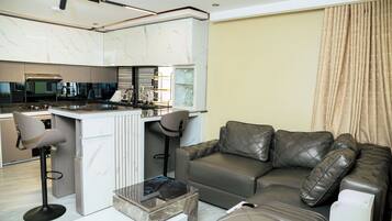 A modern kitchen with a central island, a dining area with bar stools, a leather sofa, and a coffee table.