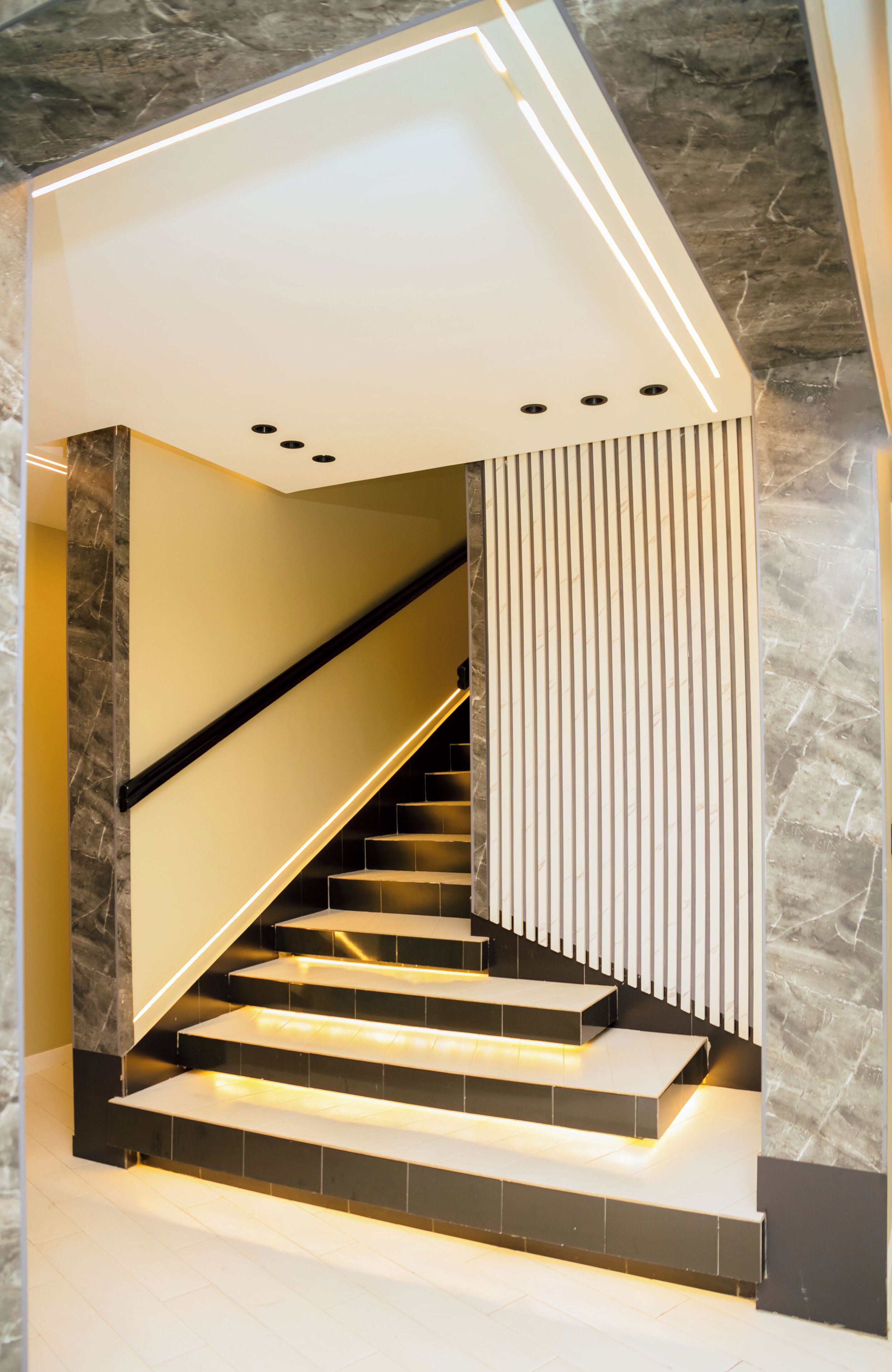 A modern staircase with integrated lighting, marble walls, and a sleek design.