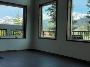 Ein Zimmer mit großen Fenstern und Bergblick, ein Balkon mit Geländer und ein Holzboden.