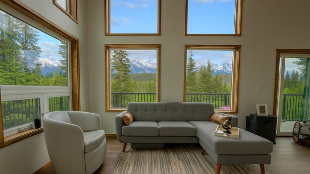 A modern living room with a grey sectional sofa, a white armchair, and a view of mountains through large windows. - Charming 2-bedroom in delightful Seward with WiFi. Not kidding friendly (Seward)