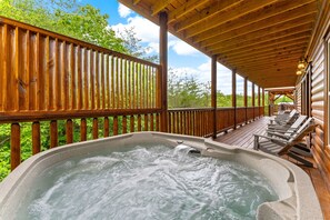 A wooden deck with a hot tub, lounge chairs, and a view of the surrounding forest. - 16 Bedrooms, 2 Heated Pools, 1 Epic Getaway (Sevierville)