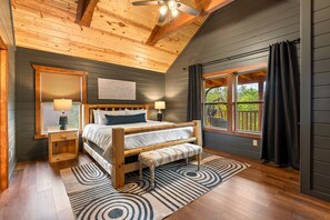 A bedroom with a wooden bed, two bedside tables, a bench, a window with curtains, and a ceiling fan. - 16 Bedrooms, 2 Heated Pools, 1 Epic Getaway (Sevierville)