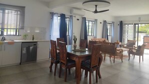 Eine geräumige Küche mit Essbereich, inklusive einem zentralen Tisch mit Stühlen, Deckenventilator und großen Fenstern mit Vorhängen.