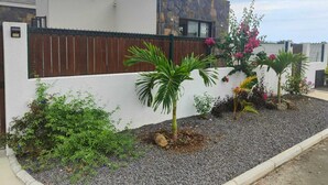 Ein modernes Haus mit weißer Fassade, einer Wand aus Naturstein und einem Kiesgarten mit verschiedenen Pflanzen und Blumen.