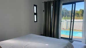Ein Schlafzimmer mit einem großen Bett, einem Fenster und Blick auf einen Swimmingpool.