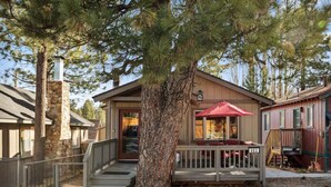 A lodge with a stone chimney, a covered deck with red furniture, and a wooden staircase leading to the entrance. - *NEW*  Alpine Crest + Pet Friendly (Big Bear Lake)