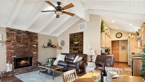 A cozy living room with a fireplace, leather sofas, a dining table with wine glasses, and a kitchen in the background. - *NEW*  Alpine Crest + Pet Friendly (Big Bear Lake)