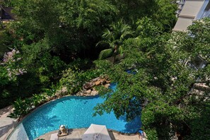 A swimming pool surrounded by lush greenery, a stone ledge, and a clear blue sky.