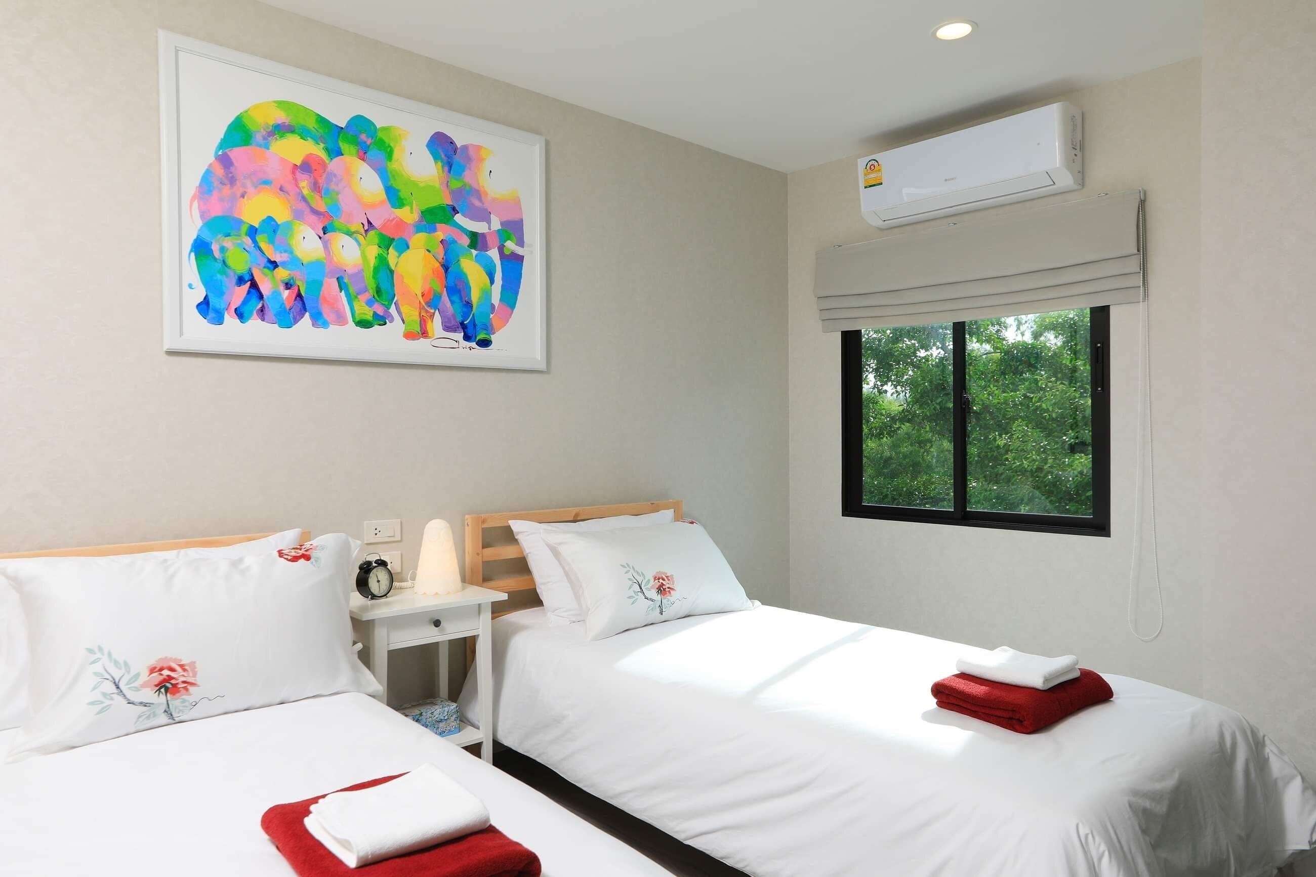 A hotel room with two beds, a large abstract painting, an air conditioning unit, and a window with a view of greenery.