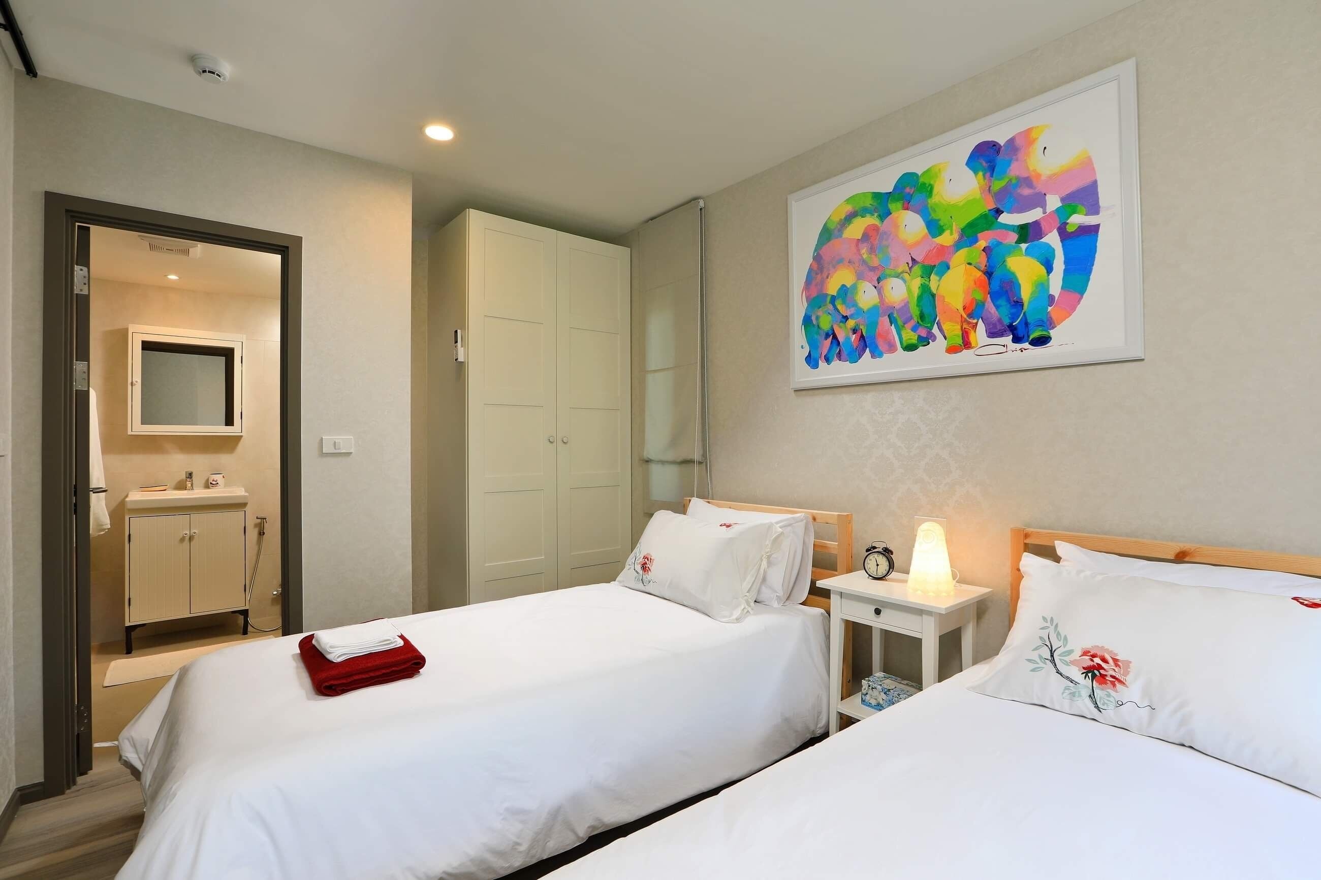 A hotel room with two beds, a bathroom, and a colorful abstract painting on the wall.