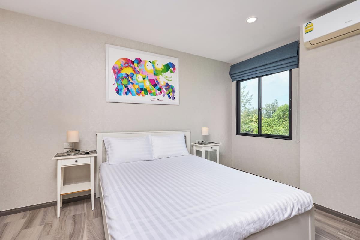 A hotel room with a bed, two bedside tables, a window with a view, and a colorful abstract painting on the wall.
