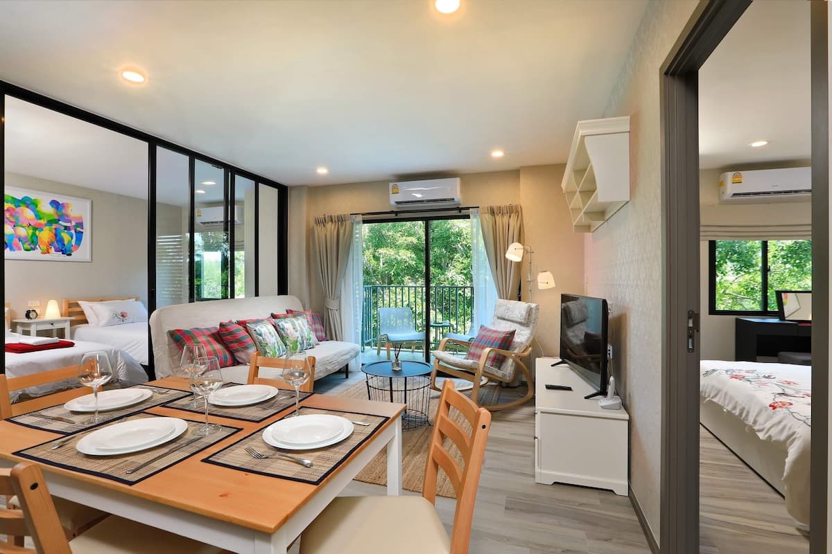 A modern hotel room with a dining area, a sofa, a TV, and an air conditioning unit.