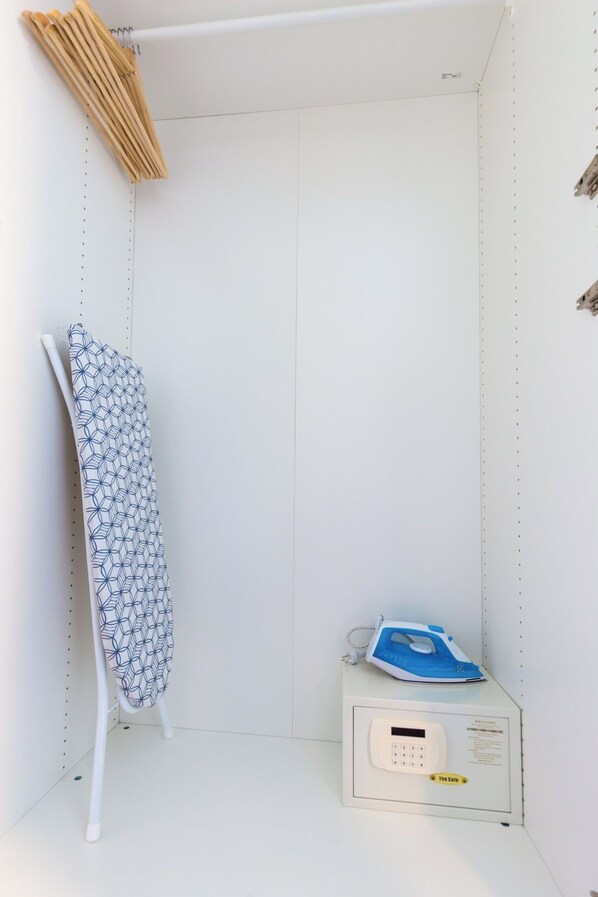 A small, white utility room with a white ironing board, a blue iron, and a digital scale.