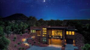 A modern house with a large glass facade, surrounded by a landscaped garden with red mulch, and a view of the night sky. - NEW Spacious 5-bedroom house with Views, Spa, Fire pit, Golf & Hammocks (Sedona)