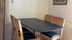 Een eethoek met een donkere tafel en houten stoelen, een lijst met een foto aan de muur, en een deur met lichtschakelaar.