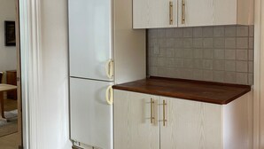 Een kleine keuken met een witte koelkast, houten kastjes en een betegelde achterwand.