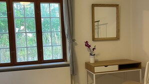 Een kamer met een bed, een bureau met stoel, een raam met gordijnen, en een spiegel aan de muur.