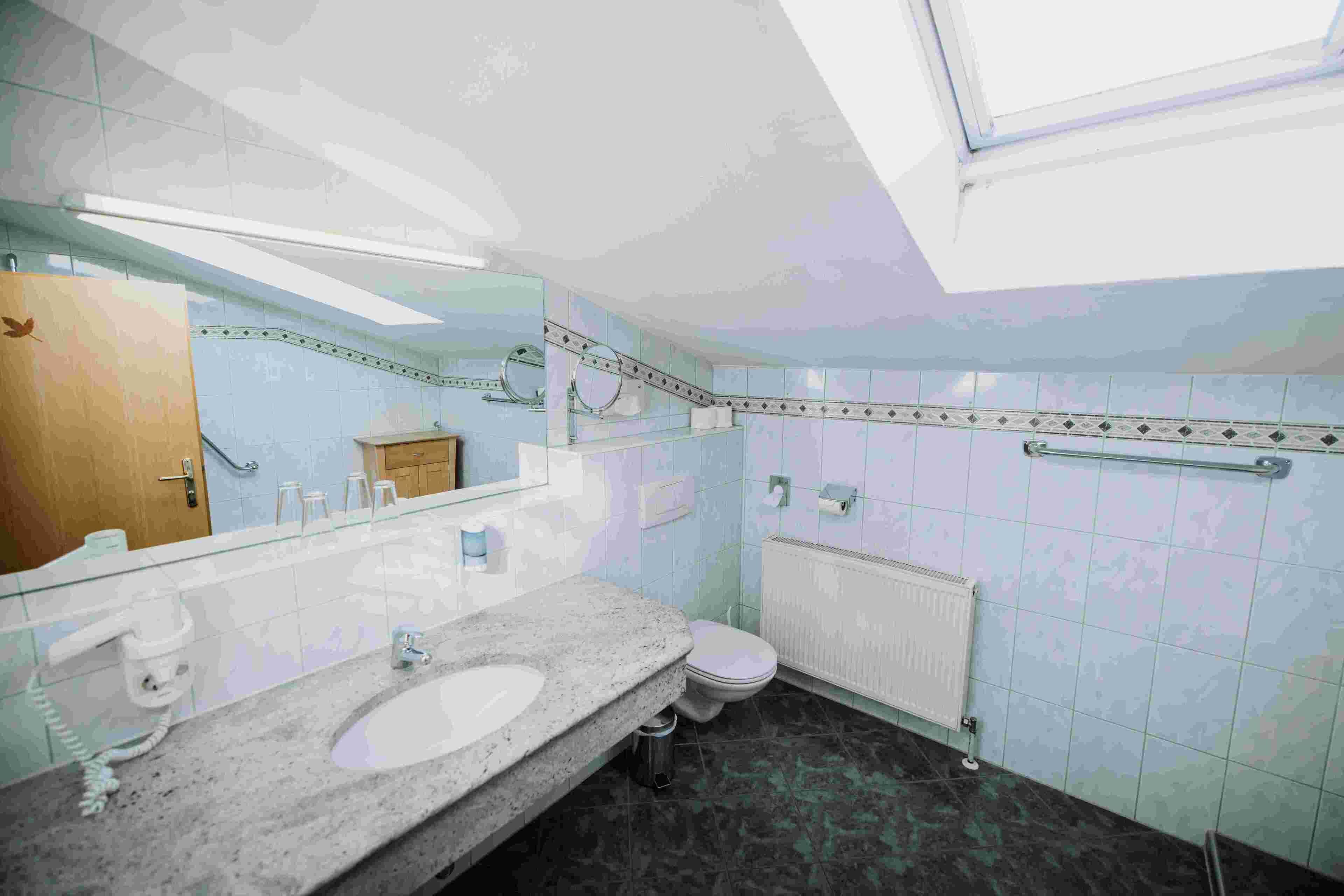 Ein Badezimmer mit großem Spiegel, Waschbecken, Toilette und Heizkörper.