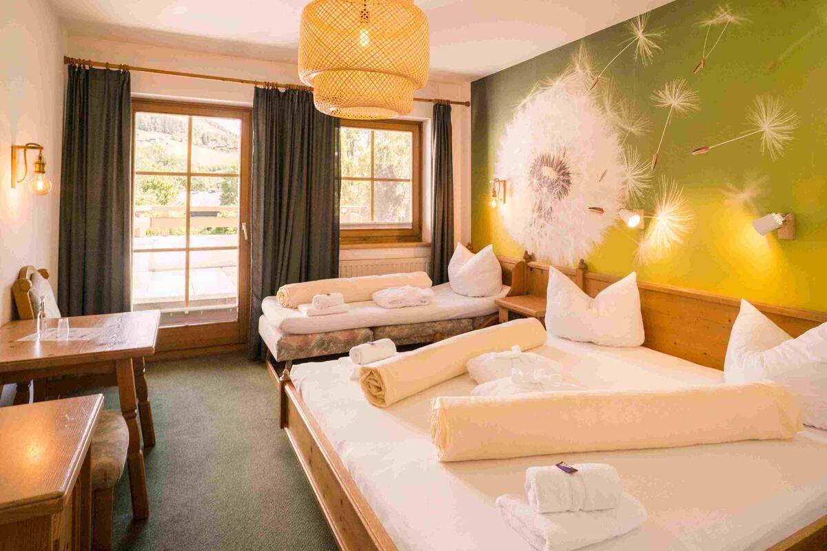 A hotel room with a large bed, a smaller bed, a desk, and a window with curtains.
